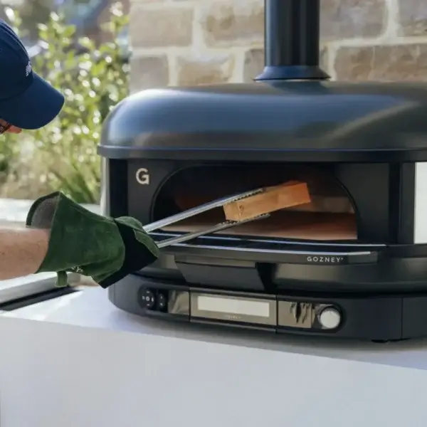 Pinzas Gozney colocadas junto a un horno exterior para pizza y fuego vivo.
