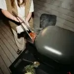 Persona usando las pinzas Gozney para mover carne en una barbacoa.