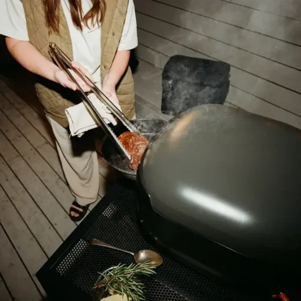 Persona usando las pinzas Gozney para mover carne en una barbacoa.