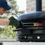 Hombre con un guante Gozney de ante introduciendo la mano protegida en un horno de pizza exterior.