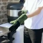 Hombre poniéndose los guantes Gozney de ante verde en una cocina exterior.