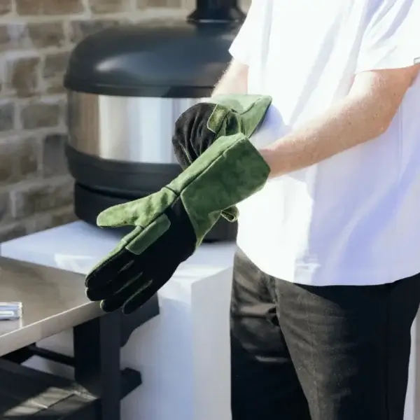 Hombre poniéndose los guantes Gozney de ante verde en una cocina exterior.