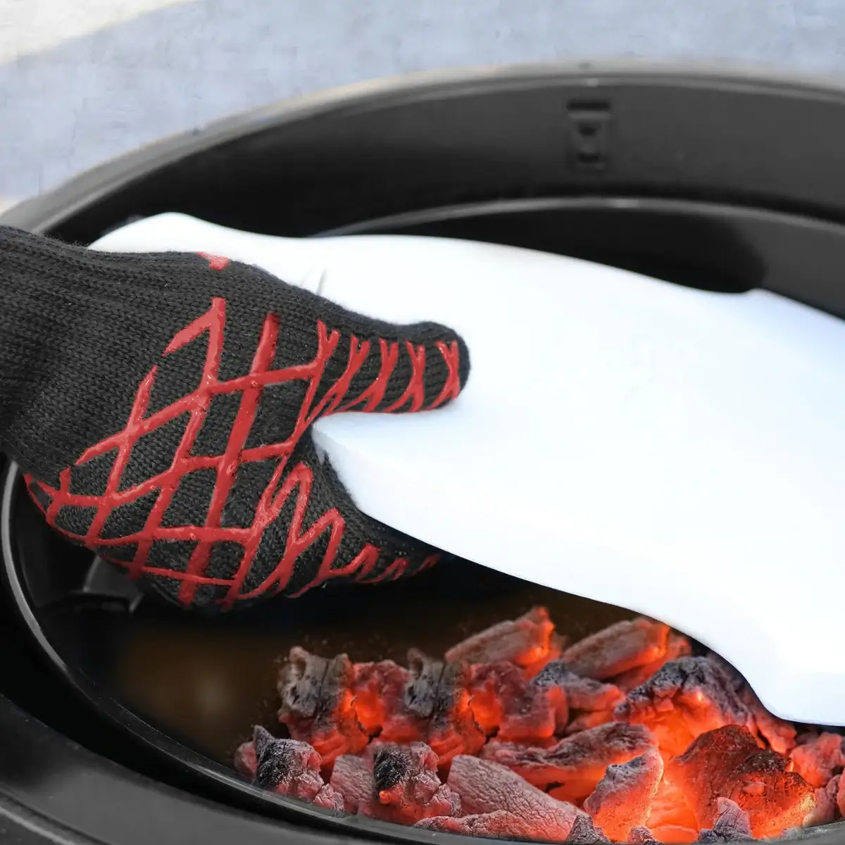 Guante para barbacoa Char-Griller manipulando un accesorio junto a las brasas