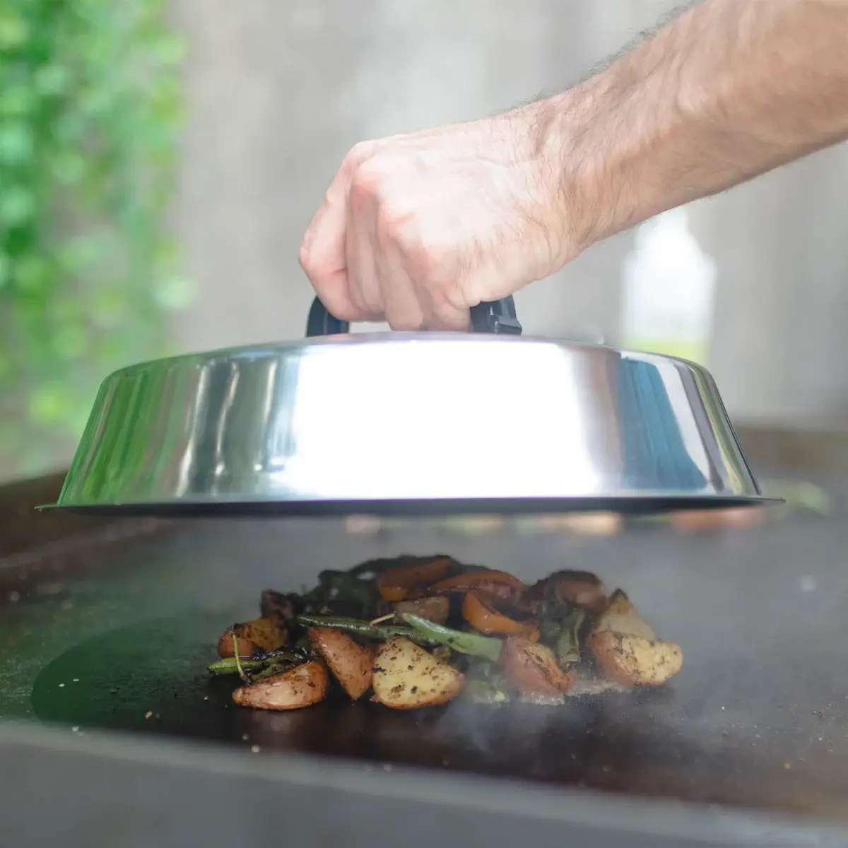 Cúpula Char-Griller cubriendo verduras y patatas sobre una plancha