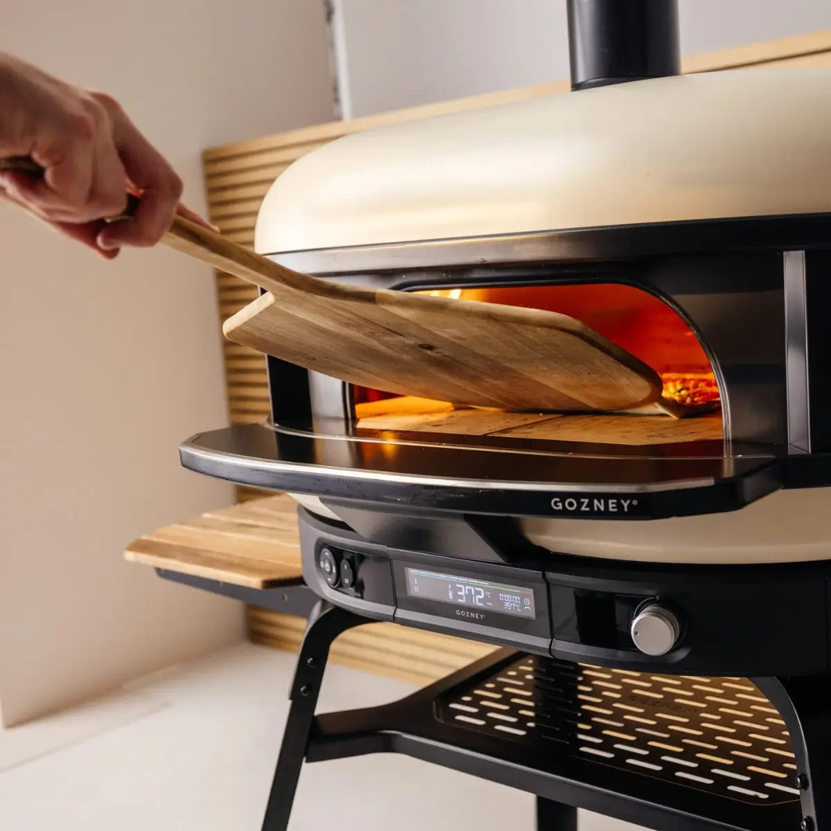 Pala de madera Gozney introduciendo una pizza en el horno
