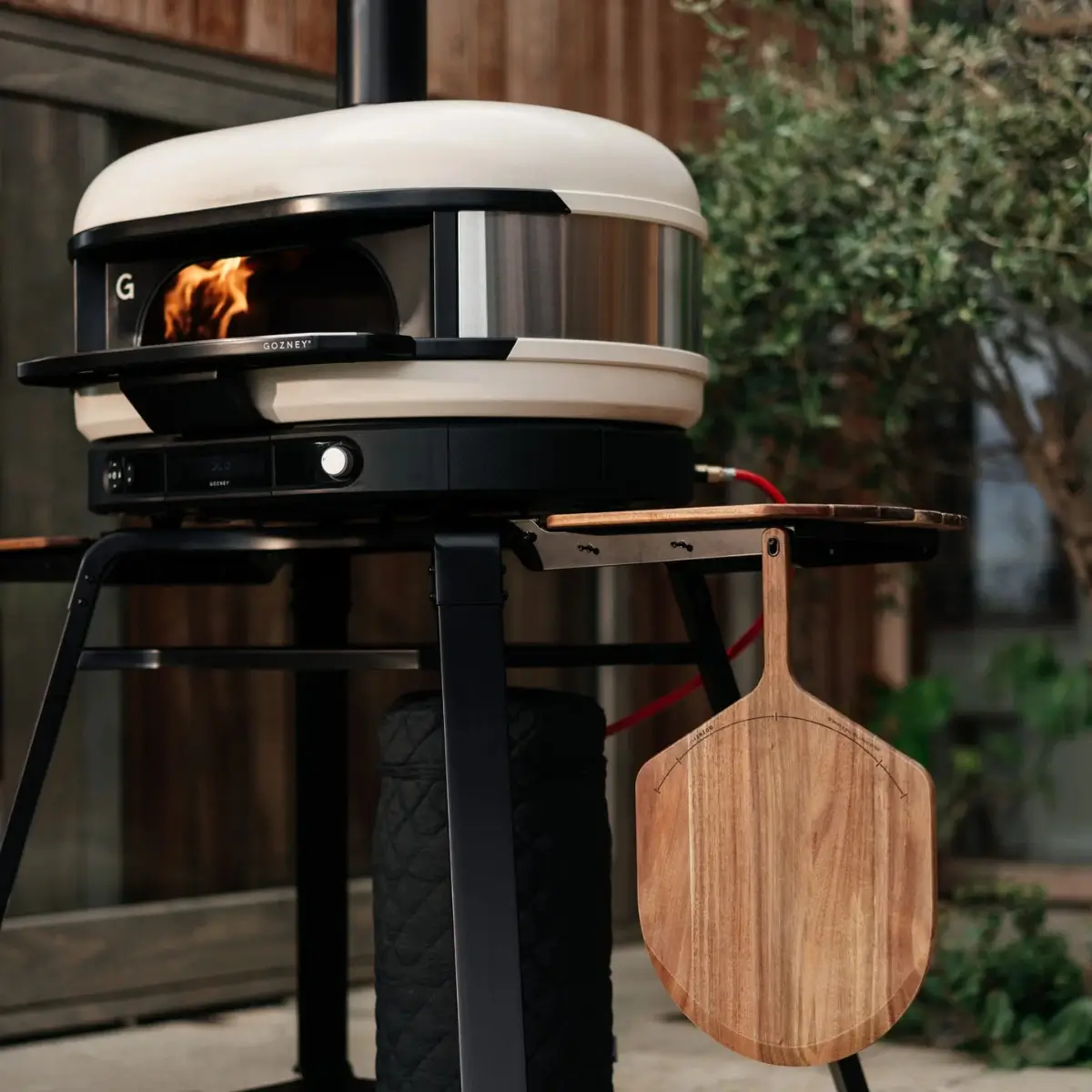 Pala de madera de acacia Gozney colgada junto a un horno de pizza
