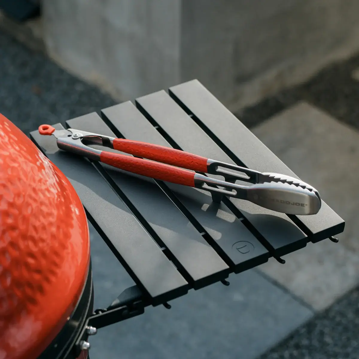 Pinzas Krafted apoyadas con la cabeza elevada sobre la mesa lateral de un Kamado Joe